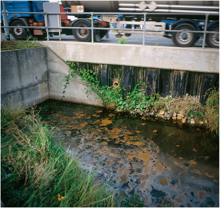Polluted stormwater runoff next to road in industrial area containing petrochemical works and storage facilities, UK.